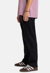 Vaqueros negros de pierna recta con una textura suave, combinados con una camiseta rosa y zapatillas marrones con rayas blancas.