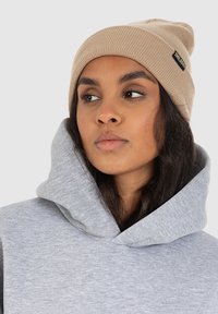 Beige ribbed beanie with a small black label. Gray hoodie with a wide, overlapping neckline and soft texture.