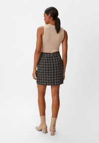 Beige geripptes ärmelloses Top, kombiniert mit einem schwarz-weißen karierten Minirock; tanfarbene Ankle Boots mit Blockabsatz runden das Outfit ab.