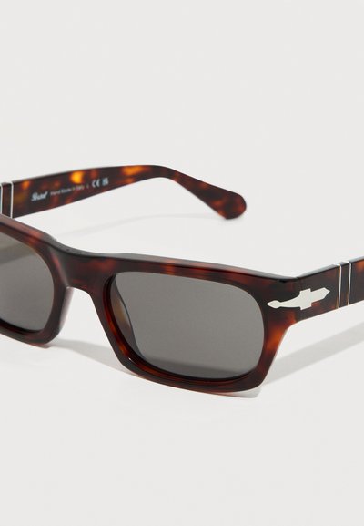 Ορθογώνια γυαλιά ηλίου με σχέδιο χελώνας, σκούρους φακούς και ασημί λεπτομέρεια σε σχήμα βέλους στα πλαϊνά, τοποθετημένα πλάγια σε λευκό φόντο.