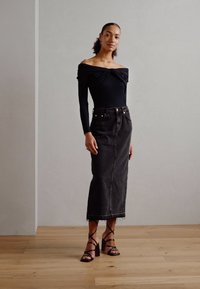 Svart off-the-shoulder bodysuit i kombination med en hög midja svart jeanskjol. Skorna består av remsandaler med blockklack.