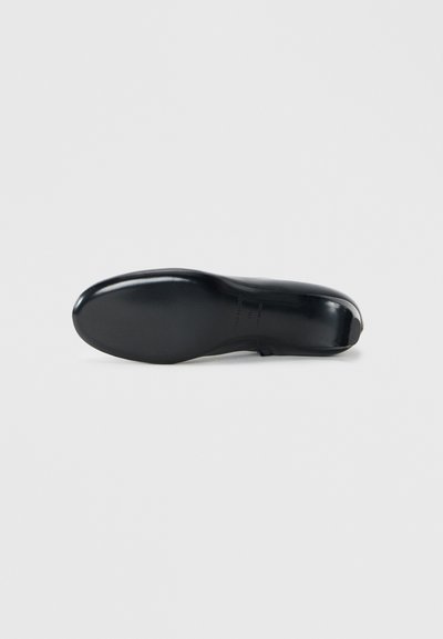 Semelle de chaussure en cuir noir, surface lisse, bout légèrement arrondi, design minimaliste, talon renforcé, avec un détail de marque près de l'arche.