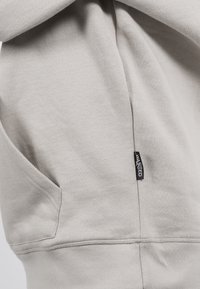 Sudadera gris claro hecha de una suave mezcla de algodón, con un bolsillo tipo canguro y un dobladillo cosido, además de una pequeña etiqueta de la marca en el lateral.