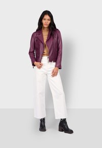 Upravená fialová kožená motorkářská bunda se zipovými kapsami, kombinovaná s béžovým tričkem a bílými kalhotami s širokými nohavicemi. Černé kotníkové boty na podpatku.