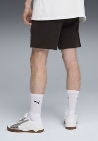 Shorts de sport noirs en coton avec une coupe décontractée, assortis à des chaussettes blanches présentant un logo noir, et des baskets blanches avec des accents argentés.