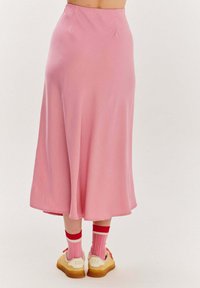 Ružová saténová midi sukňa s hladkým povrchom, rozšíreným strihom a pásom. V kombinácii s krémovými teniskami a ružovými pruhovanými ponožkami.