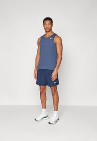 Marine tanktop og shorts, begge med hvide Nike-logoer. Modellen bærer hvide sneakers med grønne detaljer og hvide sokker. Glat stof, atletisk pasform.