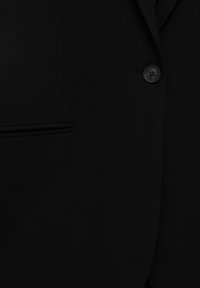 Gros plan d'une veste de costume noire montrant un seul bouton noir et une poche à fente horizontale.