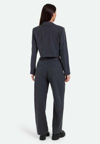 Blazer accollato grigio scuro a righe e pantaloni a gamba larga, realizzati in tessuto testurizzato. Presenta un colletto a punte e tasche laterali.