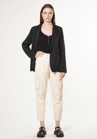 Zwarte blazer over een zwarte tanktop met knopen, gecombineerd met crèmekleurige cargobroek met zijzakken en zwarte chunky sandalen.