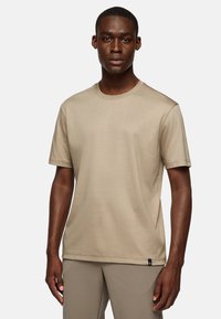 Beige short-sleeve t-shirt made of soft fabric with a crew neck, featuring a small blue accent tag at the hem. Smooth texture.