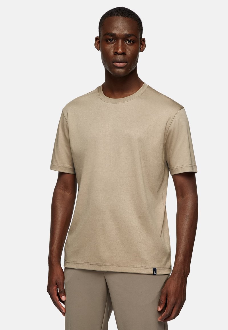 Beige short-sleeve t-shirt made of soft fabric with a crew neck, featuring a small blue accent tag at the hem. Smooth texture.