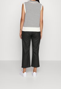 Suéter sin mangas a rayas en blanco y negro, combinado con pantalones anchos oscuros y zapatillas blancas. Diseño simple con acentos en canalé.