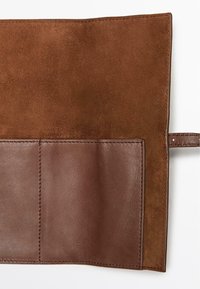 Braune Geldbörse aus Leder und Wildleder mit glatt strukturierter Oberfläche, großer flacher Tasche und einer genähten Naht entlang des Randes.