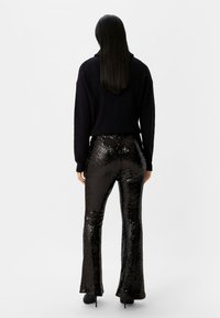 Zwarte geribbelde trui gecombineerd met glanzende zwarte pailletten flared pants. De broek heeft een gladde textuur en reflecteert licht voor extra detail.