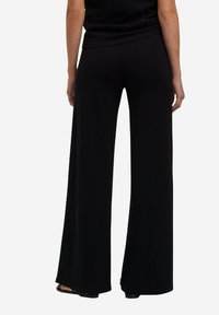 Zwarte broek met wijdvallende pijpen, gemaakt van zachte stof, met een gladde afwerking en zijnaad. Het ontwerp heeft een subtiele draping en een losse pasvorm.