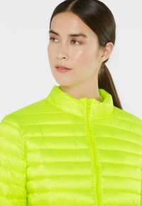 Neon yellow puffer jacket with a zippered front, high collar, and horizontal stitching for texture. Lightweight and fitted design.