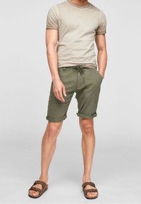 T-shirt beige en coton avec manches retroussées, associée à un short vert olive avec ourlets roulés et taille à cordon ajustable. Sandales marron.