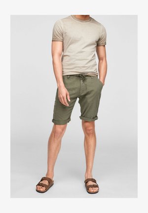 Béžové bavlněné tričko s ohrnutými rukávy, v kombinaci s olivově zelenými šortkami s ohrnutými lemy a nastavitelným pasem se šňůrkou. Hnědé sandály.