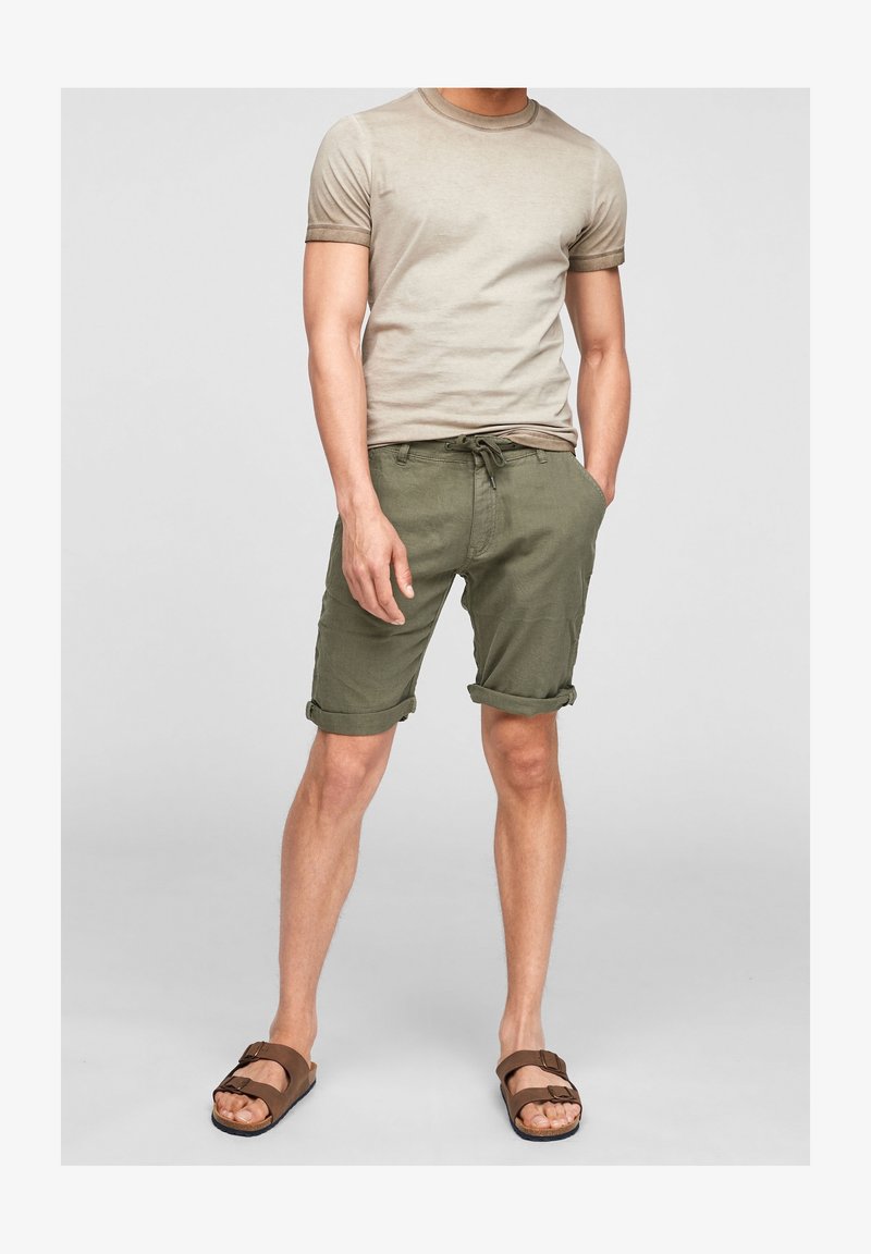 T-shirt beige en coton avec manches retroussées, associée à un short vert olive avec ourlets roulés et taille à cordon ajustable. Sandales marron.