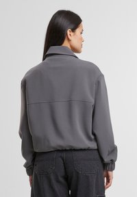 Gray collared jacket with a relaxed fit, featuring long sleeves with elastic cuffs and a smooth texture, complemented by dark pants.