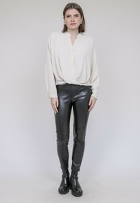 Chemisier crème à boutons, à la coupe décontractée, associé à un pantalon en cuir noir ajusté et des bottines noires. Textures lisses et détails minimaux.