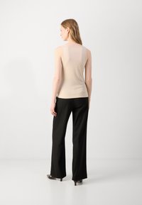 Beige sleeveless top with a fitted design and smooth texture, paired with black wide-leg trousers and heels. Simple and elegant silhouette.
