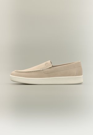 Mocasini beige slip-on cu talpă albă din cauciuc, design minimalist și detaliu discret de cusături, arătați în profil lateral pe un fundal neutru.