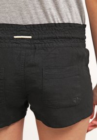 Pantaloni corti neri in lino con fascia in vita arricciata, due tasche posteriori e un cordoncino decorativo bianco. Tessuto liscio, design casual.