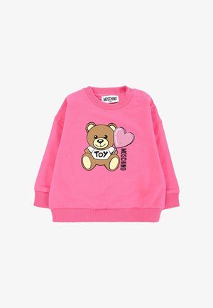 Sweatshirt rose pâle pour bébé avec un ours en peluche tenant un ballon en forme de cœur pailleté, « TOY » sur la chemise de l'ours et le texte « MOSCHINO » à côté.