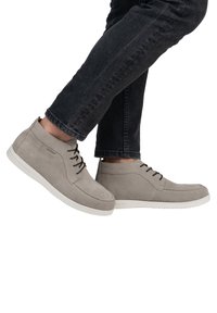 Stivaletti alla caviglia in suede grigio chiaro con lacci neri, suole in gomma bianche e dettagli di cucitura ridotti, indossati con jeans scuri.