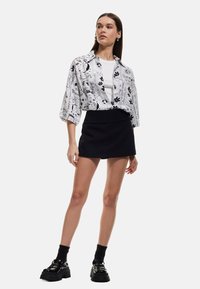 Camicia oversize a righe bianche e nere con maniche corte, indossata sopra una maglietta bianca e abbinata a una mini gonna nera e scarpe nere chunky.