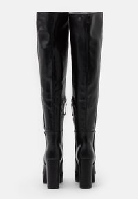 Bottes hautes en cuir noir jusqu'aux genoux, au design ajusté, avec talons carrés et fermetures éclair latérales. Texture lisse avec une finition brillante.