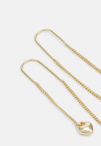 Boucles d'oreilles en or avec crochets allongés, présentant de délicates chaînes et un petit pendentif en forme de cœur. Texture lisse, finition brillante et design léger.