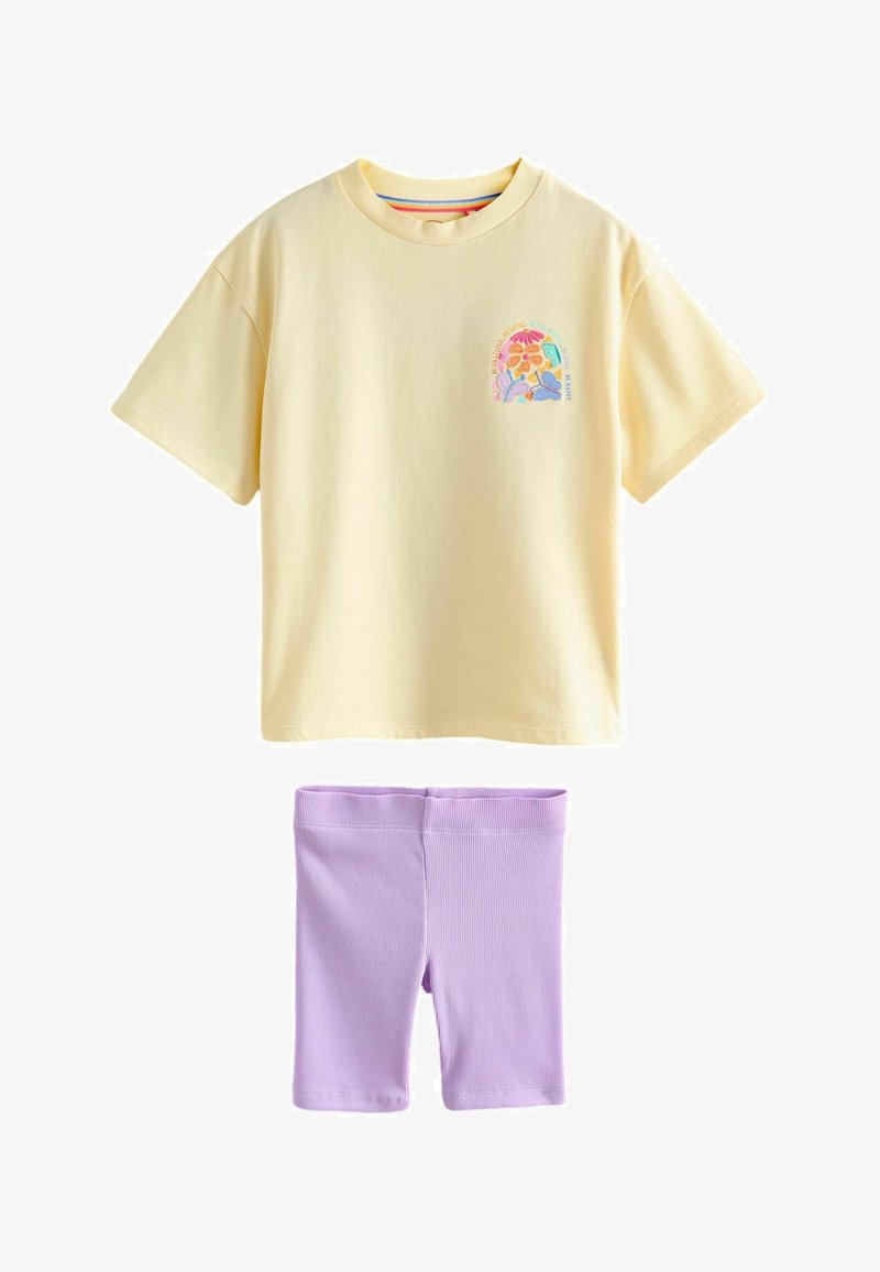 Geel T-shirt met korte mouwen en een klein kleurrijk bloemmotief op de borst, gecombineerd met geribbelde lichtpaarse shorts tot op de knie.