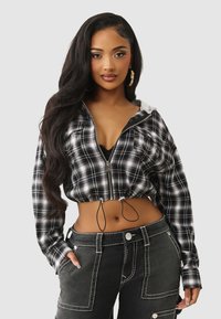 Przycięta, czarno-biała, kraciasta bluza z kapturem na zamek, z paskiem ściągającym w talii, zestawiona z czarnymi spodniami o wysokim stanie, ozdobionymi białymi szwami i kieszeniami.