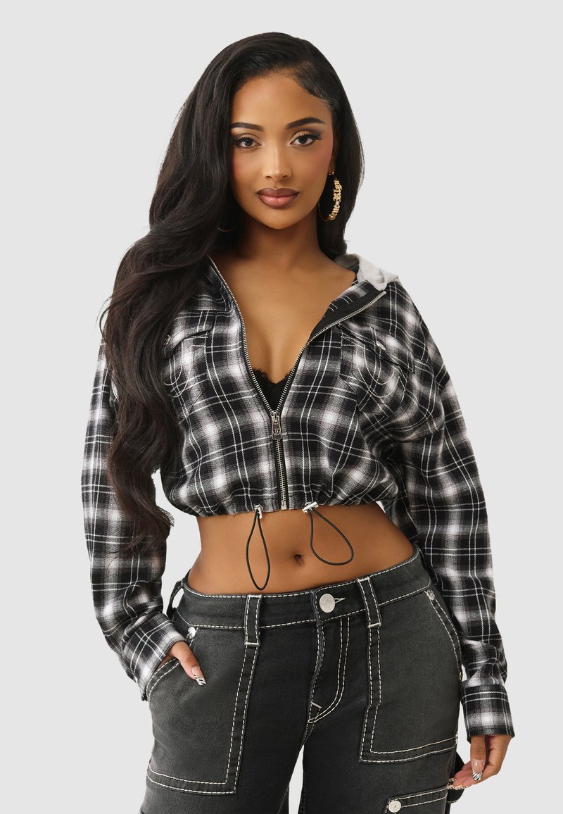 Przycięta, czarno-biała, kraciasta bluza z kapturem na zamek, z paskiem ściągającym w talii, zestawiona z czarnymi spodniami o wysokim stanie, ozdobionymi białymi szwami i kieszeniami.