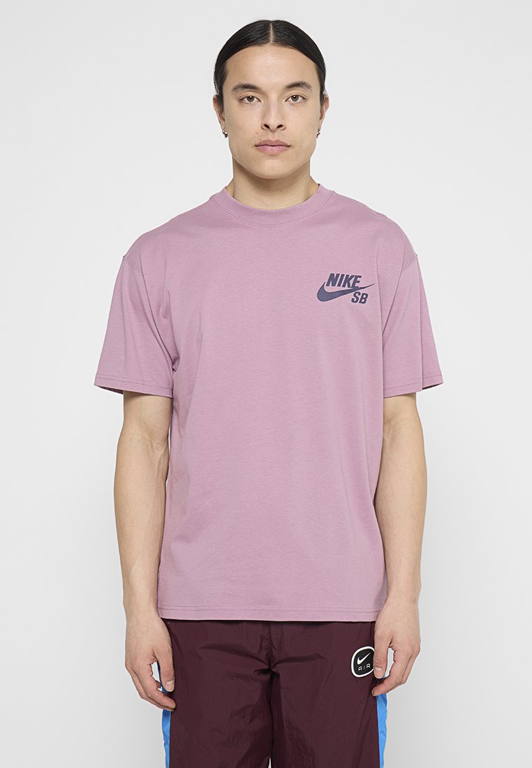 Liliowa koszulka z krótkim rękawem wykonana z bawełny, z granatowym logo Nike SB na lewej piersi. Prosty krój z okrągłym dekoltem, gładka tekstura.