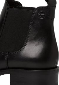 Botín negro de cuero a la altura del tobillo con paneles laterales elásticos, textura suave y tacón bajo. Detalle del logo visible cerca del tacón.