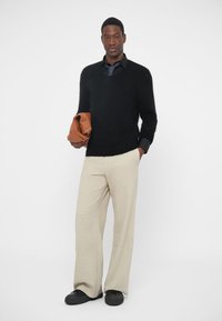 Maglione di lana nero, pantaloni beige a gamba larga e scarpe slip-on nere; tiene una borsa di pelle marrone; colori solidi, vestibilità casual, texture morbida.