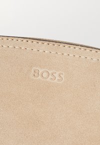 Béžový zamatový materiál s jemnou textúrou. Názov značky "BOSS" je vyrazený na povrchu a podél okraja je kontrastný šev.