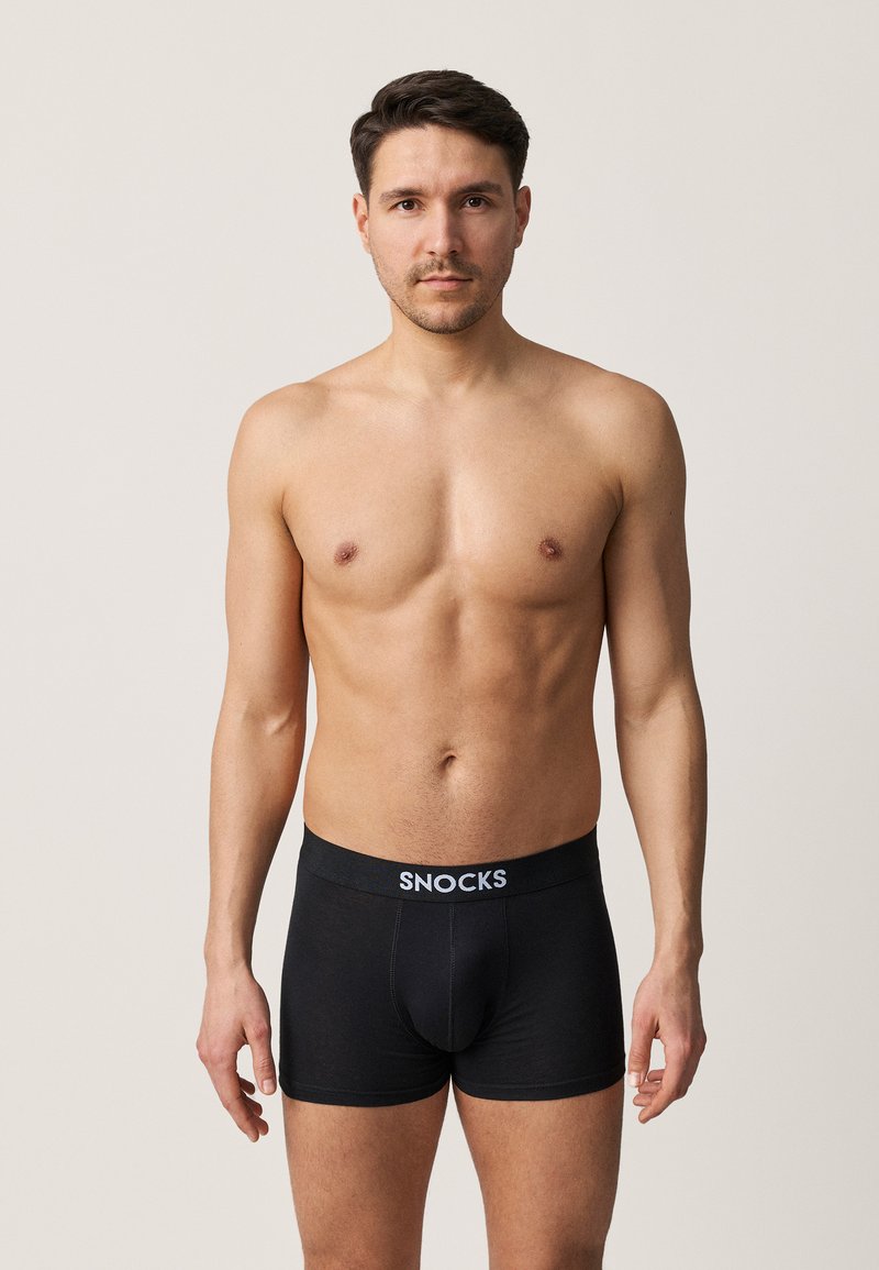 Schwarze Baumwollboxershorts mit enganliegendem Schnitt, die ein graues "SNOCKS"-Logo am Bund aufweisen, getragen von einem Modell ohne Oberteil.