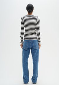 Top noir et blanc à manches longues à rayures côtelées, associé à un jean en denim bleu clair taille haute, présentant des jambes droites et des poches arrière.