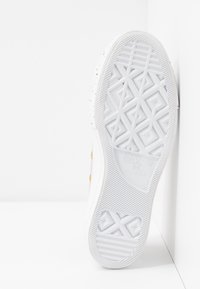Suela de zapatilla blanca de goma con patrones geométricos texturizados. Presenta el logo de la marca y pequeños acentos dorados. Acabado suave y diseño duradero.