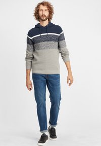 Felpa con cappuccio caratterizzata da un design a righe navy, grigio e bianco. Realizzata in tessuto a maglia testurizzata, abbinata a jeans blu e sneakers nere.