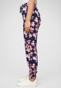 Blomster joggebukser i marineblå med rosa og hvit blomsterprint, elastisk midje og elastiske mansjetter. Kombinert med hvite joggesko.