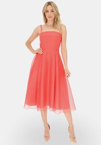 Koronkowa sukienka midi w kolorze koralowym z cienkimi ramiączkami, dopasowanym stanem i rozkloszowaną, przezroczyną spódnicą. Gładka tekstura z zwiewnym krojem, bez wyraźnych wzorów.