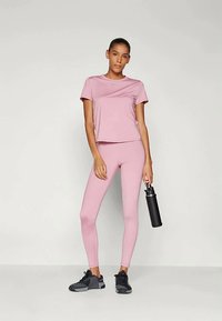 Helles pinkes Sport-T-Shirt und Leggings aus dehnbarem Material, kombiniert mit schwarzen Sportschuhen und einer schwarzen Wasserflasche.