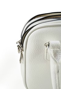 Witte, gestructureerde leren tas met twee zwarte en beige ritssluitingen en een gestikte schouderband met zilverkleurige hardware.