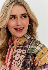 Prošívaná bunda s kombinací květinových a kostkovaných vzorů v růžové, zelené a hnědé barvě, vysokým límcem a zipovým zapínáním.